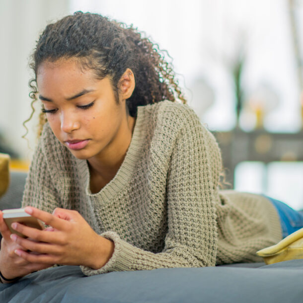 A teenage girl texts on her phone while lying on her bed.